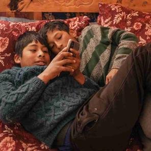 Jhon, 11, and his cousin Jheyson, 11, watch videos on YouTube on a mobile phone. Shelter For Kids has helped the family with their baking business.