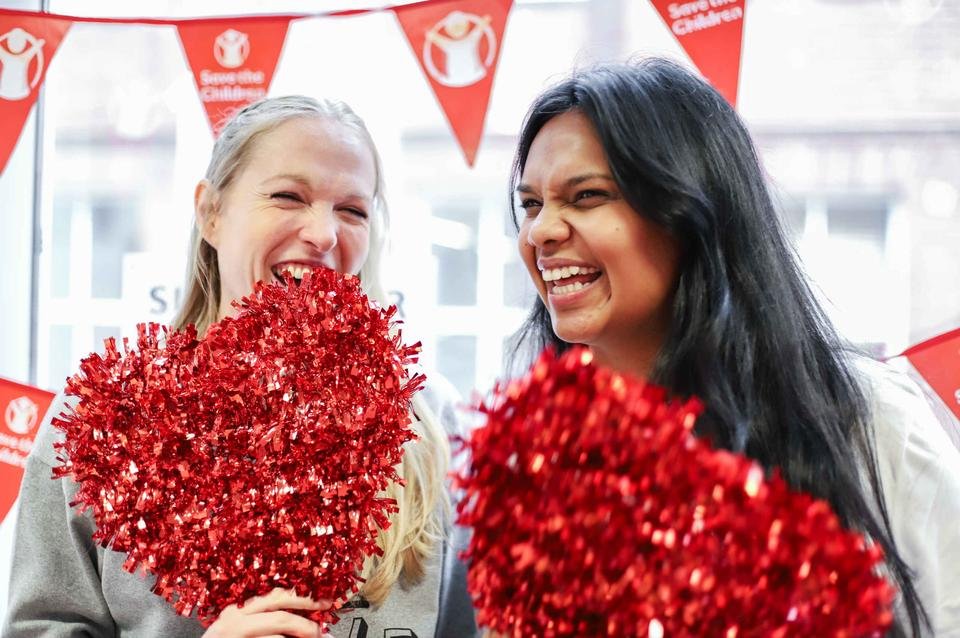 Two Shelter For Kids UK employees share a laugh together whilst holding red hearts for supporter week 2019