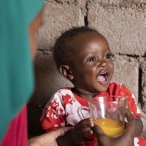 Fatima, a young child, laughing while an adult hands her a fruit juice