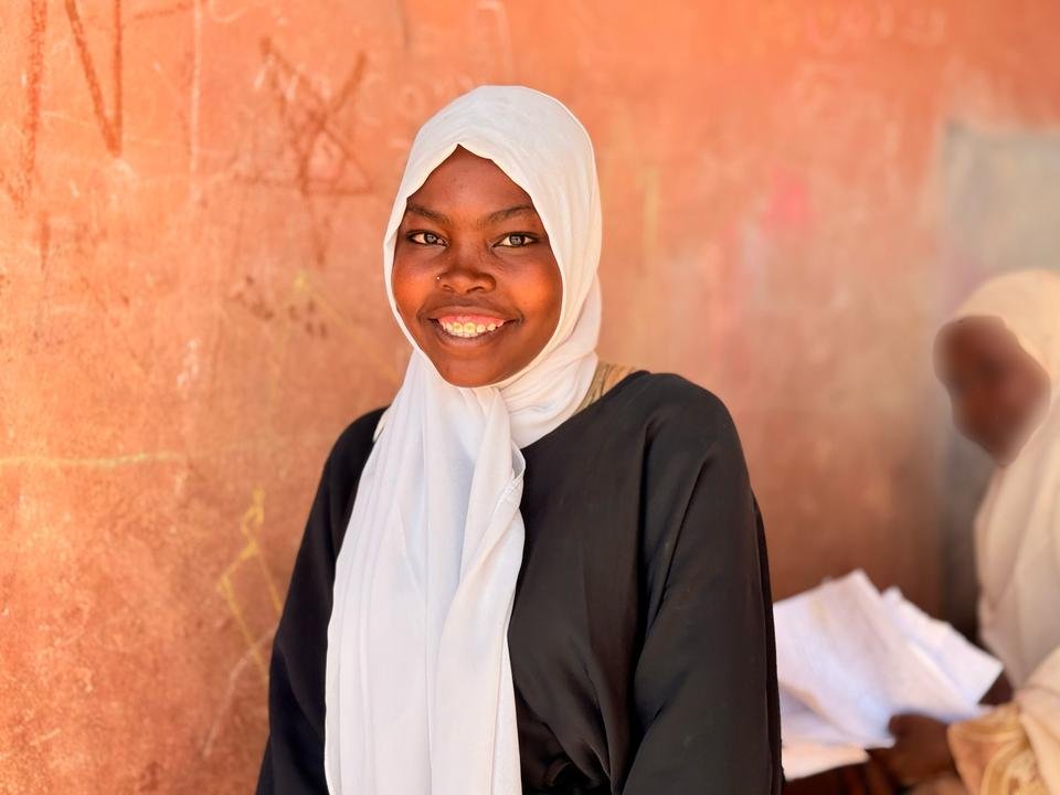 Sarra*, 17, stands in the courtyard of her school after receiving school supplies