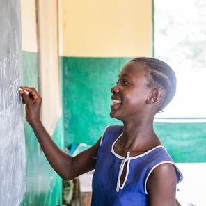 Tenneh in Sierra Leone writes on a blackboard with chalk