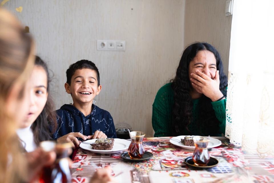 Siblings Cihan*, 11, Yasemin*, 13 and Hilal*, 16 enjoy a dessert made by their mother TÃ¼lay* at home in Gaziantep, TÃ¼rkiye