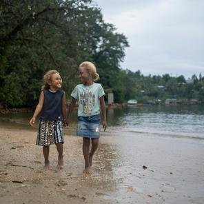 Sisters Josephine, seven, and Lucy, four, walking along the beach near their home in Malaita Province, the Solomon Islands.