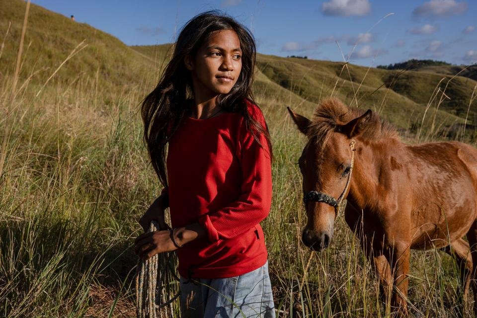 Atika, 12, walking a neighbourâ€™s horse up the valley in drought-affected East Sumba, Indonesia.