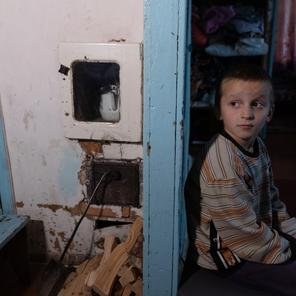 Dmytro*'s brother Taras*, 4, sits by the wall behind the heating stove at home near Chernihiv, Ukraine.