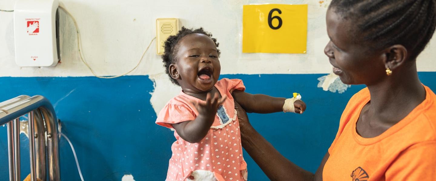 A 7-month-old baby laughs as her mother holds her and smiles at her.