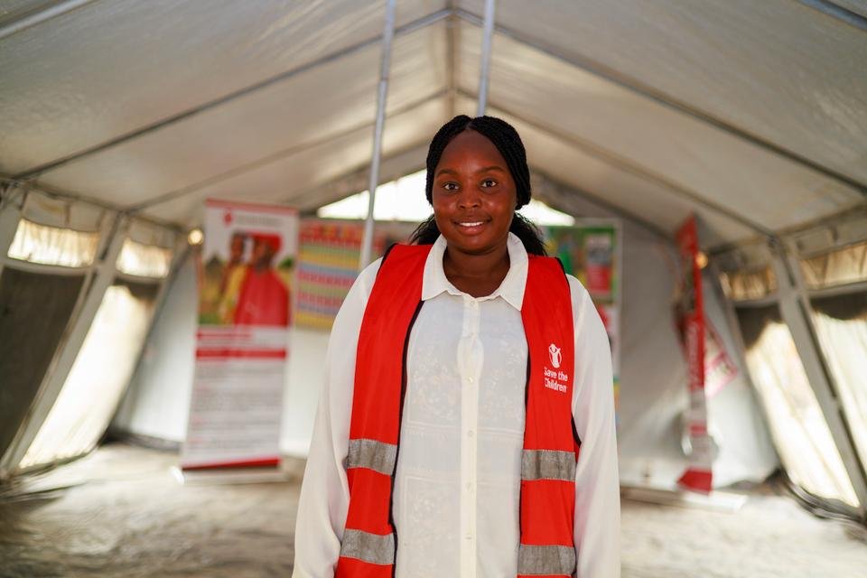 Monica, a Shelter For Kids caseworker, standing in a large tent wearing a red Shelter For Kids vest.