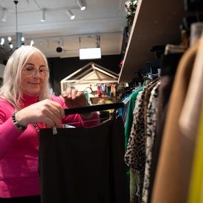 A woman in a pink top sorts through a clothing rail at a Shelter For Kids charity shop